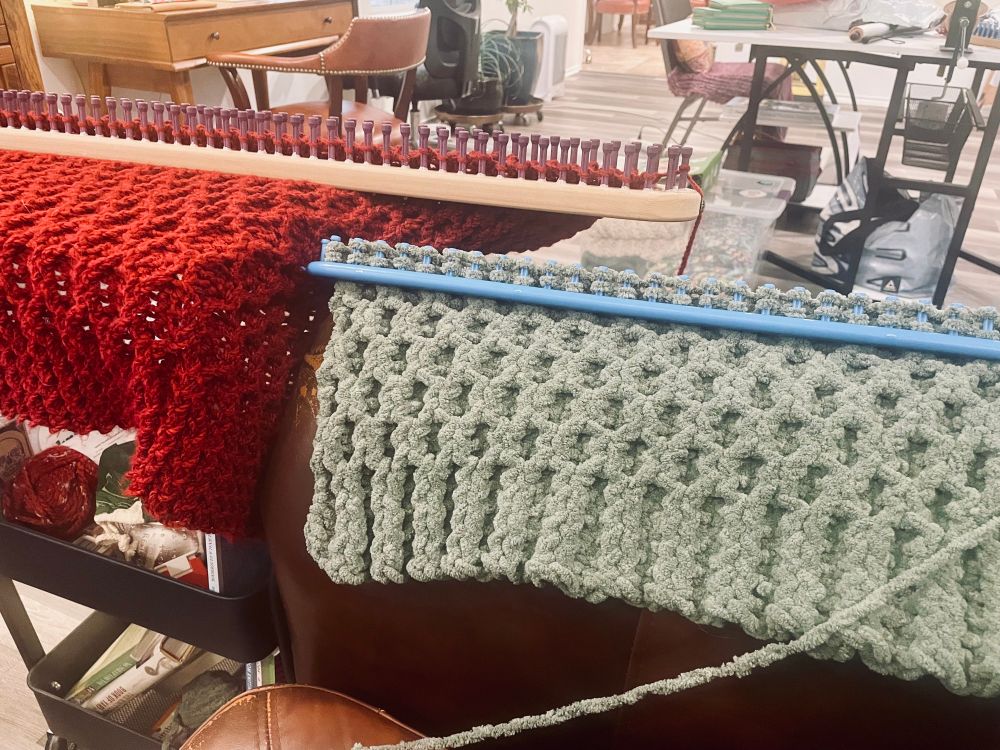 Two shawls being knit on looms. On the left is a red one on a VERY long loom, and on the right is a green one. 