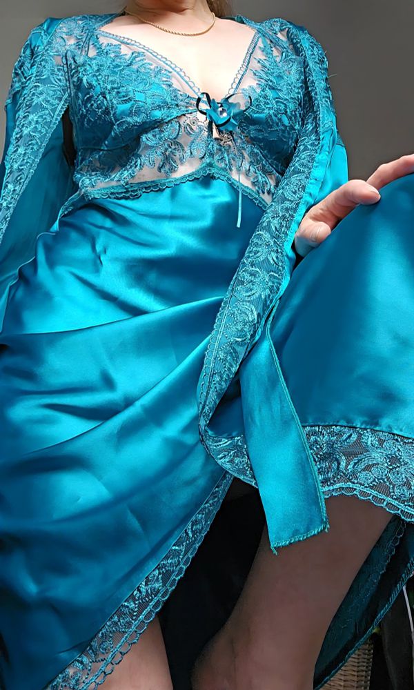 Woman wearing a teal green satin and lace  slip and robe. The delicate lace upper is adorned with a ribbon and jewel.