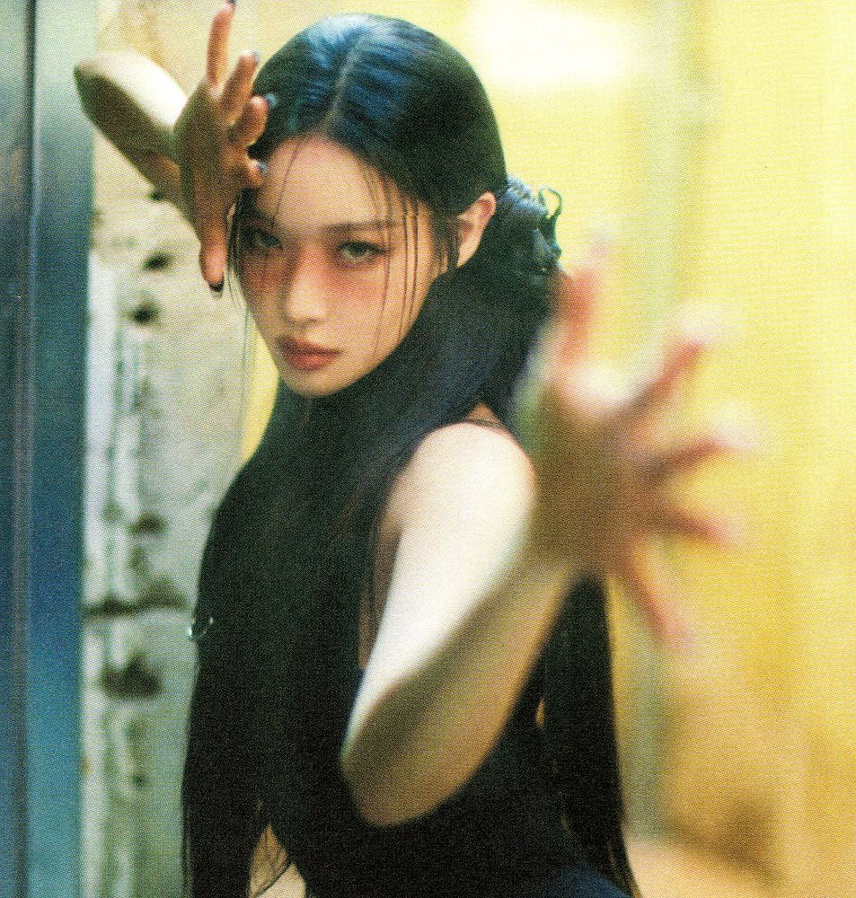 Kpop soloist CHUNGHA for 'Alivo' posing in a black dress, long hair half-tied in the back. she is reaching with her open hands towards the camera.