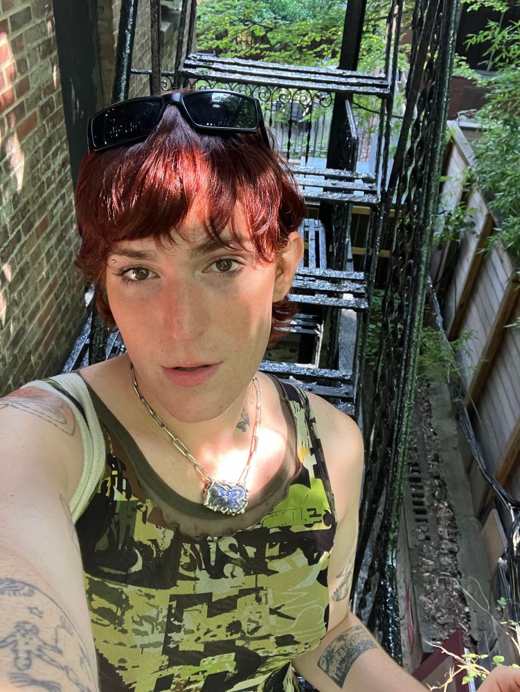 Kit in a mod green dress on a fire escape in Midtown in golden late afternoon light. She’s looking into the camera flushed and sultry with a post sex glow in the face. 