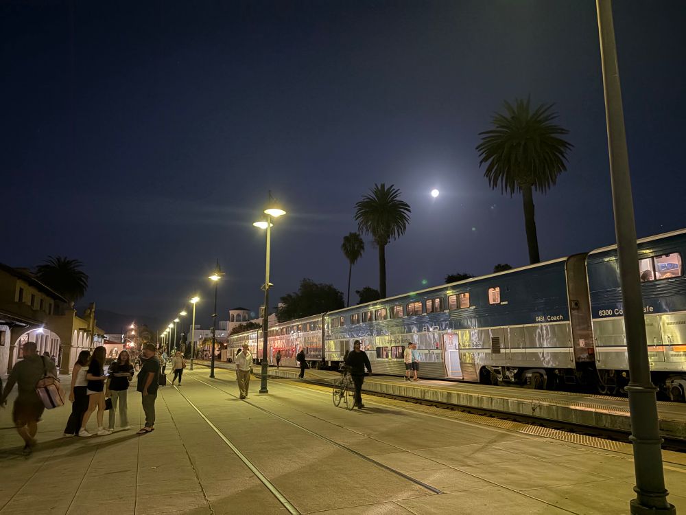 People just alighted from a Pacific Surfliner train under a nearly full moon and tall palms at Santa Barbara.