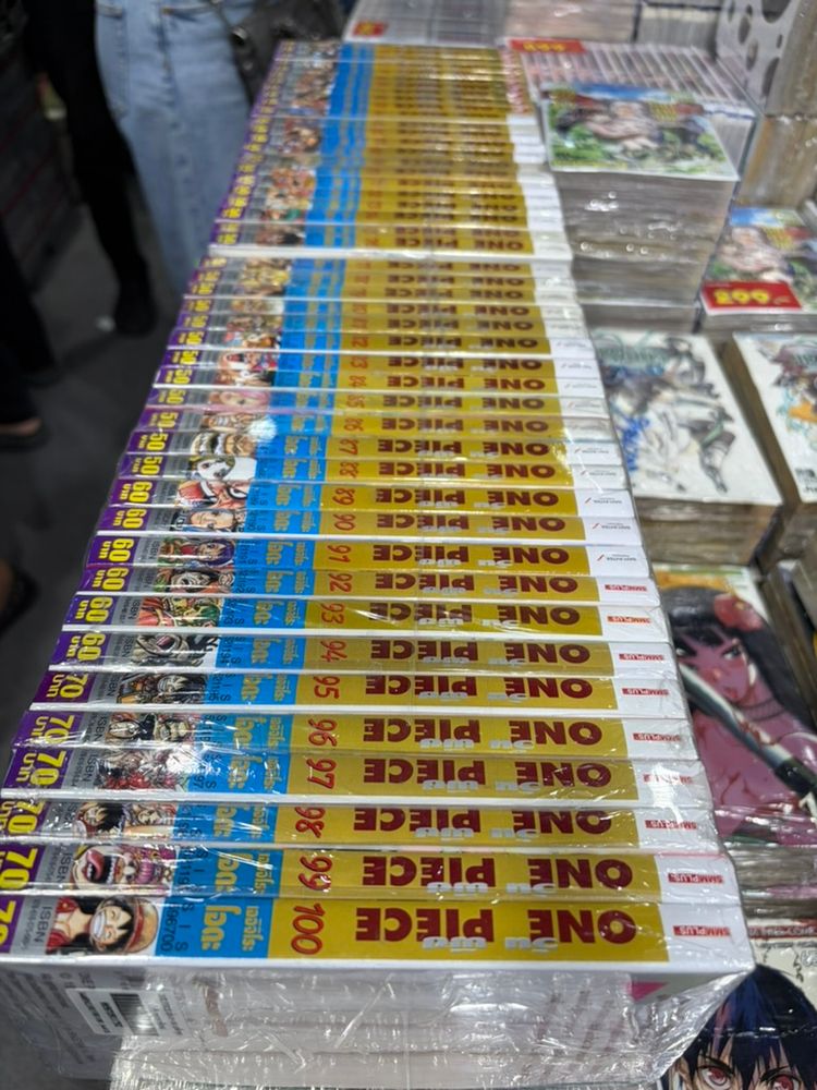 "One Piece" manga volumes up to the 100th, priced 50-70 Thai baht each. Stacks of manga sets.