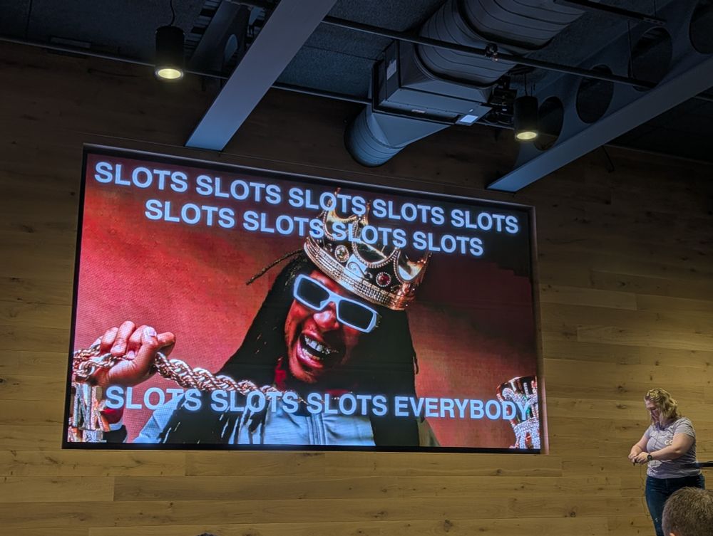 Abby micing up next to a slide with Lil Jon wearing a crown, sunglasses, holding chains with "Slots, Slots, Slots, Everybody!" in white text over the photo