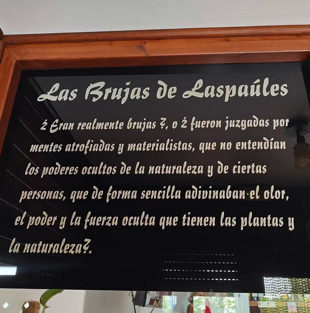 Cartel de un comercio en el que se lee: Las Brujas de Laspaúles. ¿Eran realmente brujas?, ¿O fueron juzgadas por mentes atrofiadas y materialistas, que no entendían los poderes ocultos de la naturaleza y de ciertas personas, que de forma sencilla adivinaban el olor, el poder y la fuerza oculta que tienen las plantas y la naturaleza?