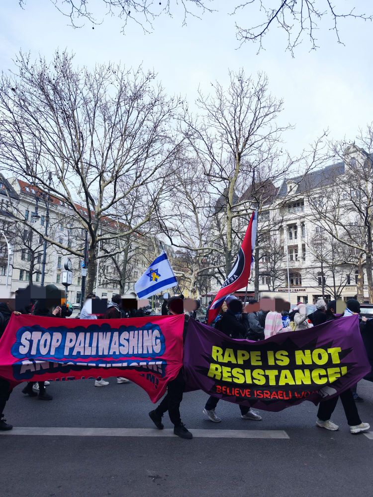 Antifaschistische Demonstration gegen den Al Quds-Tag. Auf Banner ist zu lesen "Stop Paliwashing Antisemitism. Fight Islamism." sowie "Rape Is Not Resistance. Believe Israeli Women". Dahinter weht eine Antifa-Fahne und eine israelische Fahne mit gelber Schleife.