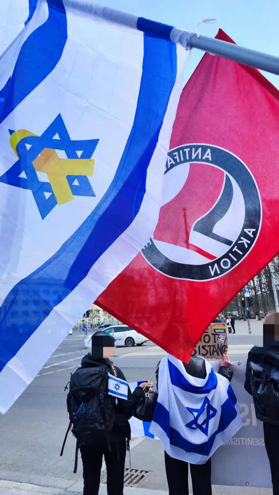 Eine Antifa-Fahne weht neben einer israelischen Fahne mit gelber Schleife bei einem Anti-Hamas Protest am Brandenburger Tor.