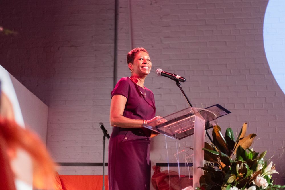 Speaker Adrienne Adams smiles in front of a podium at a gala at the Chocolate Factory Theater.
