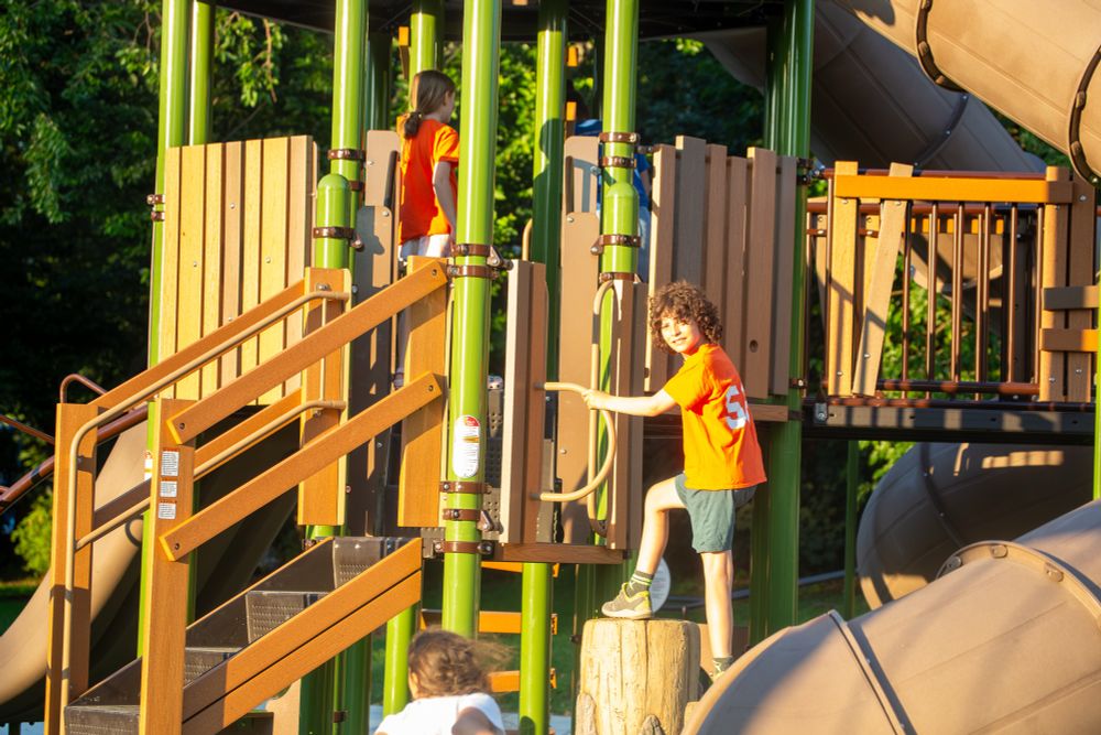 Kid wearing orange shirt climbing on new playground structure. 