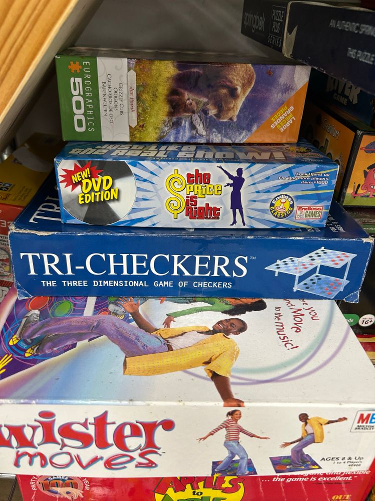 A stack of games at a thrift store, one called Tri-Checkers, the three dimensional game of checkers