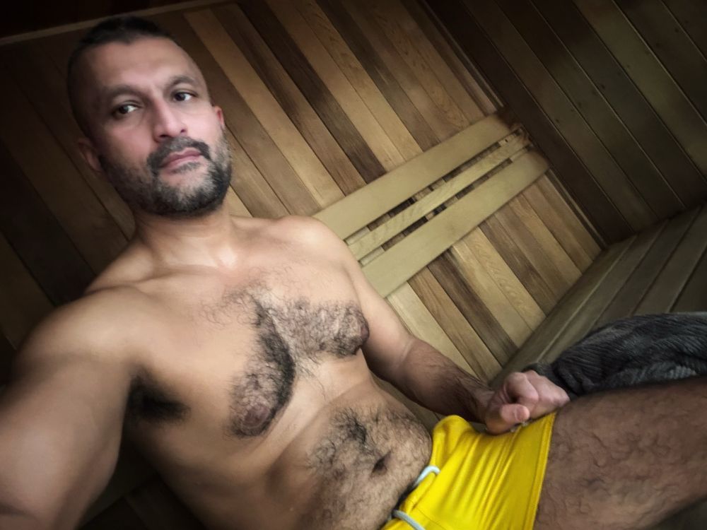 A man in a sauna wearing yellow swimming togs.