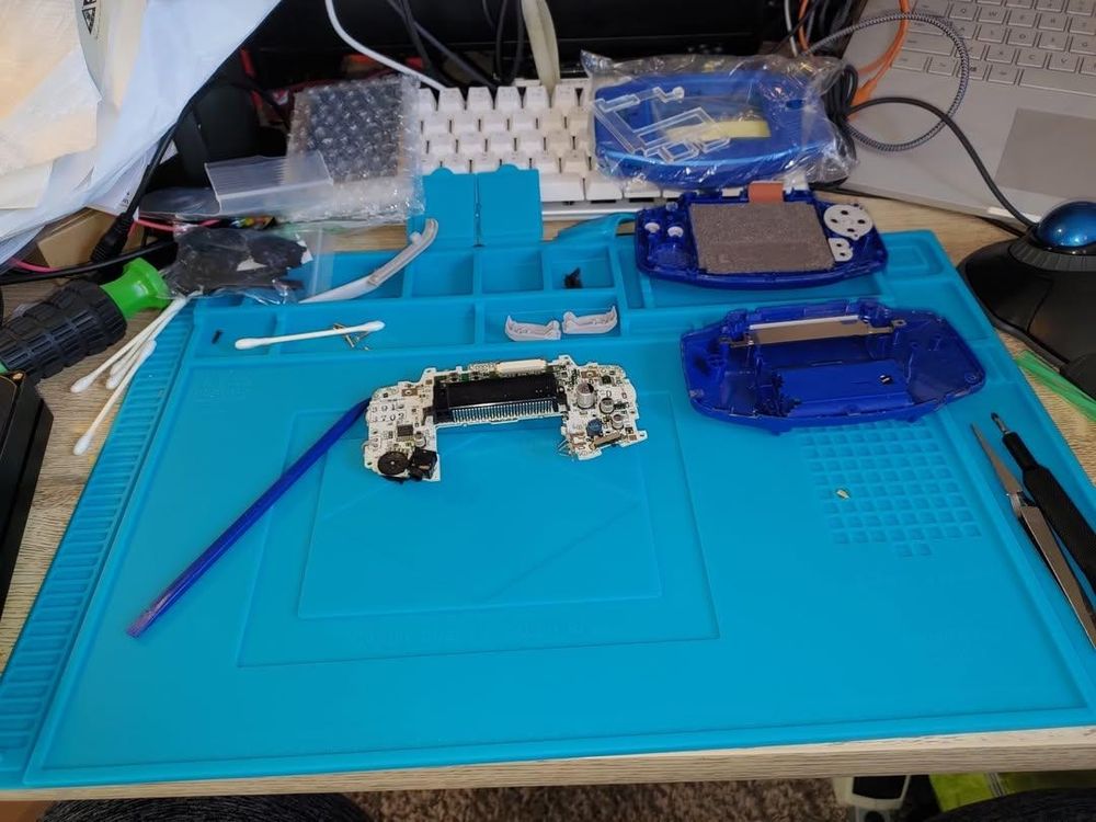 My game boy advance on a rubber mat, opened up with its motherboard exposed and all of the parts displayed. The new shell and new screen are just up to the top. 

Please ignore my messy desk