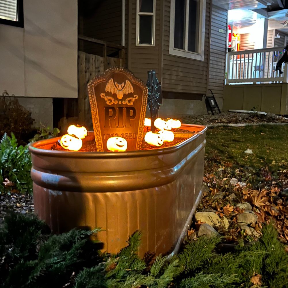 A darkly lit copper coloured trough with two menacing headstones surrounded by glowing pumpkin heads.