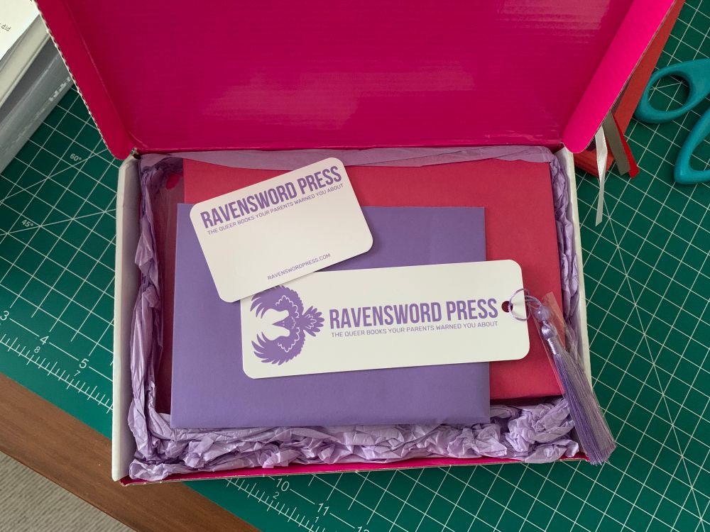 Inside the opened box, with purple, red, and fuchsia paper accents, plus a bookmark and a business card.