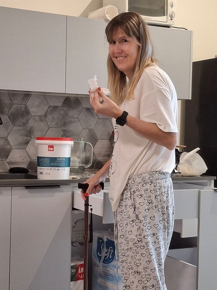 Tall cute blonde woman with a cane standing in the kitchen holding a cloth