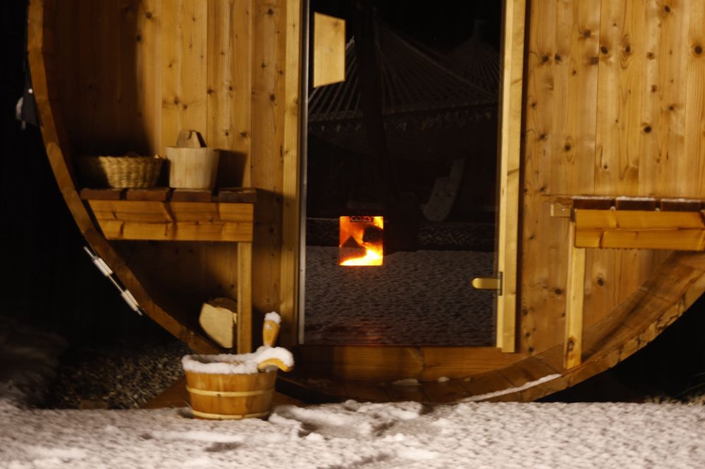La porte vitrée du sauna, derrière, le feu dans le poêle, devant, le petit seau avec la louche pour verser de l’eau sur les pierres. Le tout sous la neige