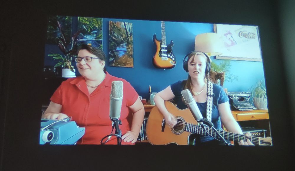 Marian Call sings and plays the guitar as Kelsey Bryce Riker plays the typewriter.