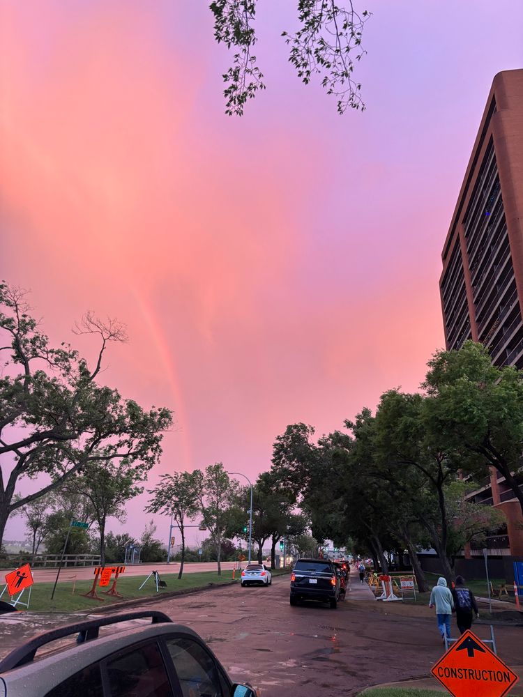 A view of the setting sun, a sky of pink and purple with a rainbow appearing through the clouds.