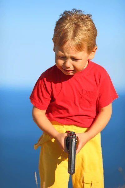 Child holding a handgun, looking away and crying. 