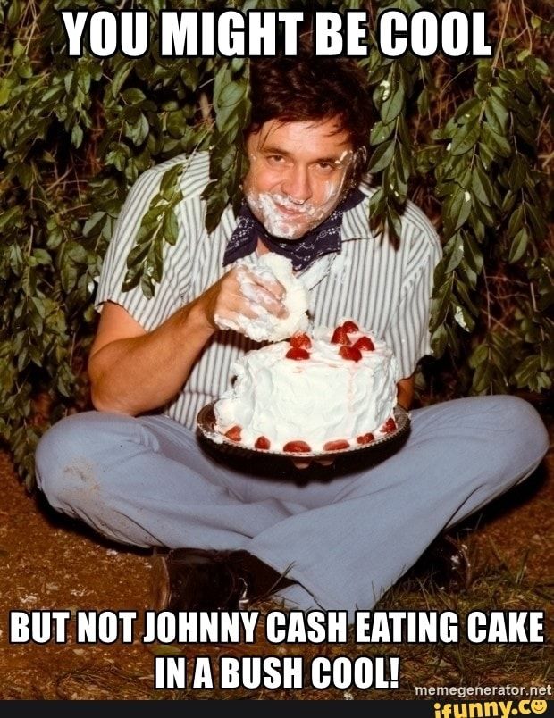A very high johnny cash eats a whole full sized iced cake with his hands, sat in a bush 