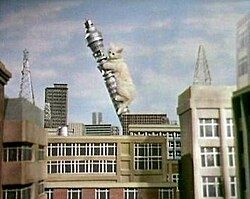 A giant white kitten climbs up the London Post office tower, collapsing it
