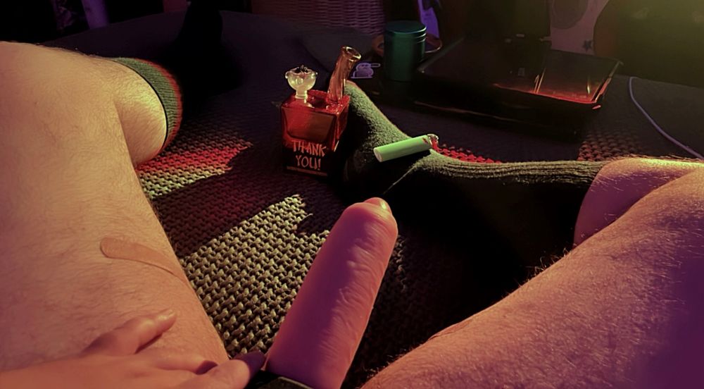 Another photo of my dick. I’m laying back with my legs open in low sunset lighting. There’s a small bong by my right foot and a lighter rested on top of it