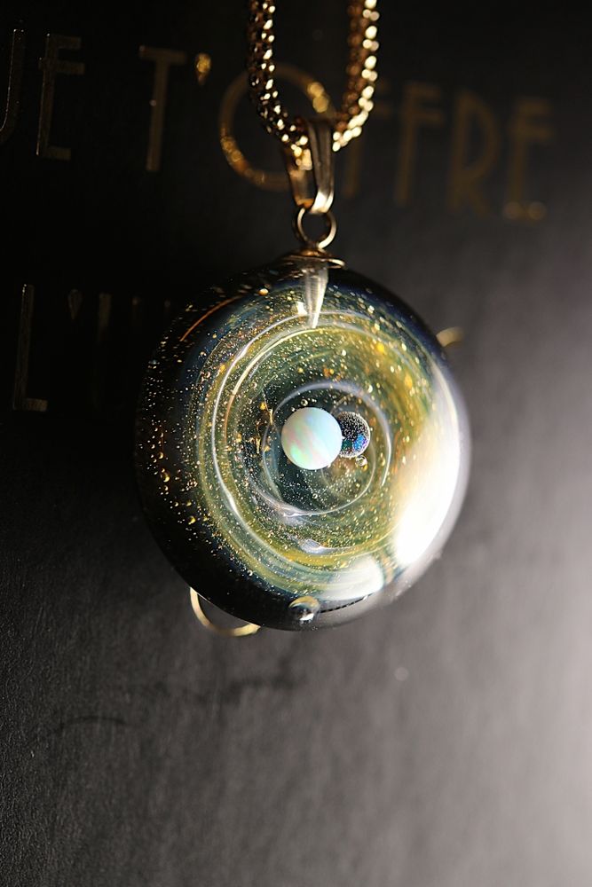 Nouveau pendentif galaxie que j’ai réalisé et qui représente un mini univers dans du verre de couleur or avec deux planétes en apesanteur .