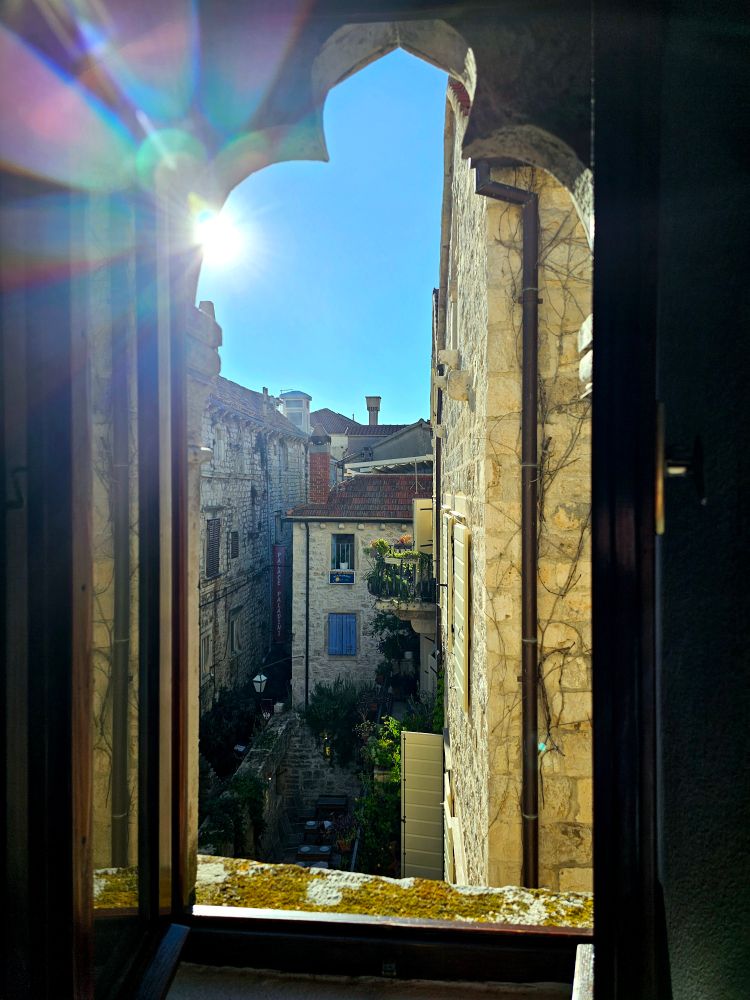 The sun peeks through an ornate window. Hvar is in the background. 