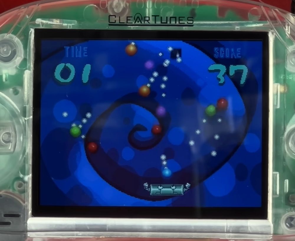 A game being played on a Cleartune prison handheld - The game being played is about deflecting balls with a paddle. The number font used for the timer and the score is the same as the one used in the Pikmin series