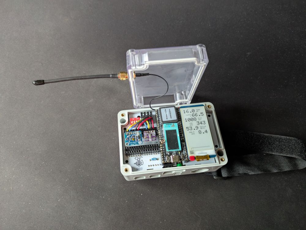 Photo of a sensor box that has been opened. An antenna is attached to the lid, and all the electronics inside the box are visible. There's a small e-ink display showing readings from the various sensors.