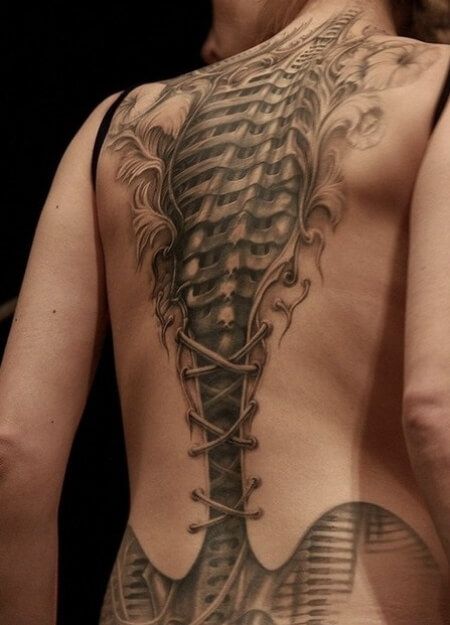 Lady's back with a corset like tattoo that has biomechanical spine underneath