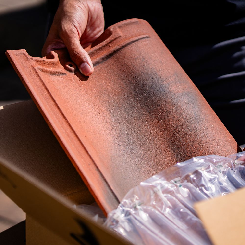 A close-up of a hand holding a terracotta roof tile.