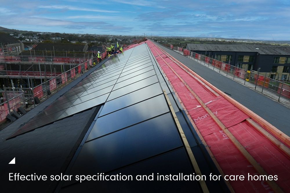 Workers on a rooftop installing solar panels at a care home, with a clear sky and distant landscape in the background.