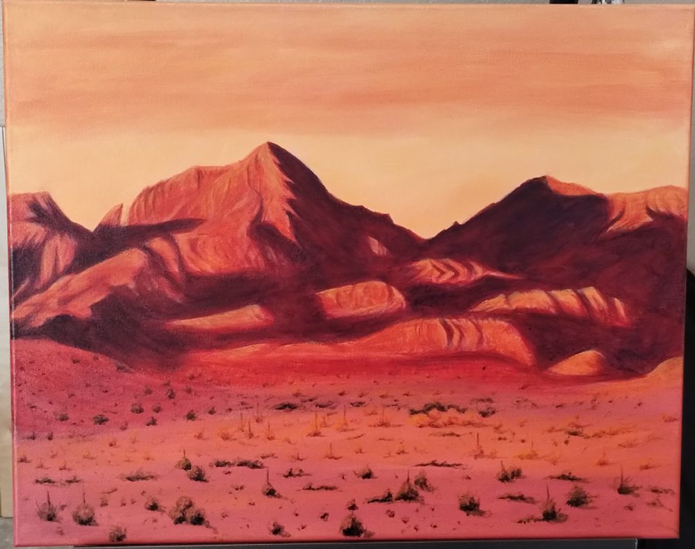 Acrylic painting on canvas of a range of rocky desert mountains, a sunset, and scrubland in the foreground. The painting is 16 by 20 inches. 