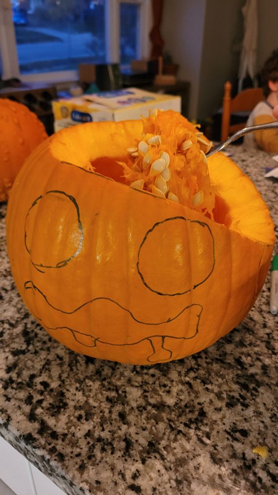 The top of the pumpkin head has been removed and the gooey pumpkin brains are being scooped out with a metal spoon. 