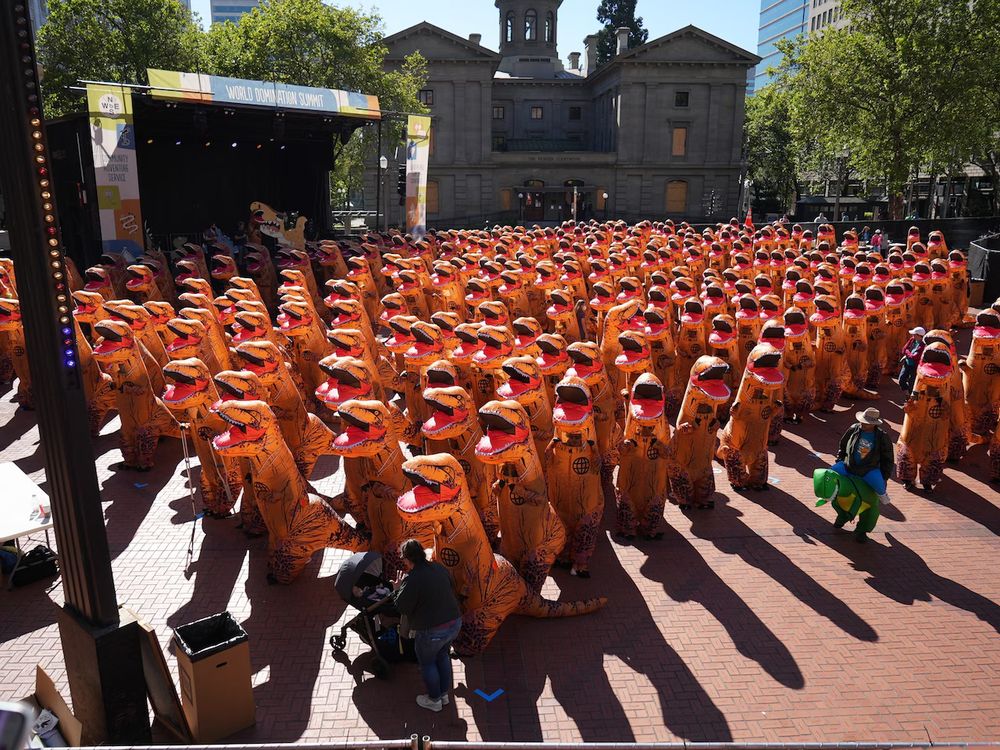 Hundreds of people wearing inflatable T rex costumes stand in Portland's Pioneer Square