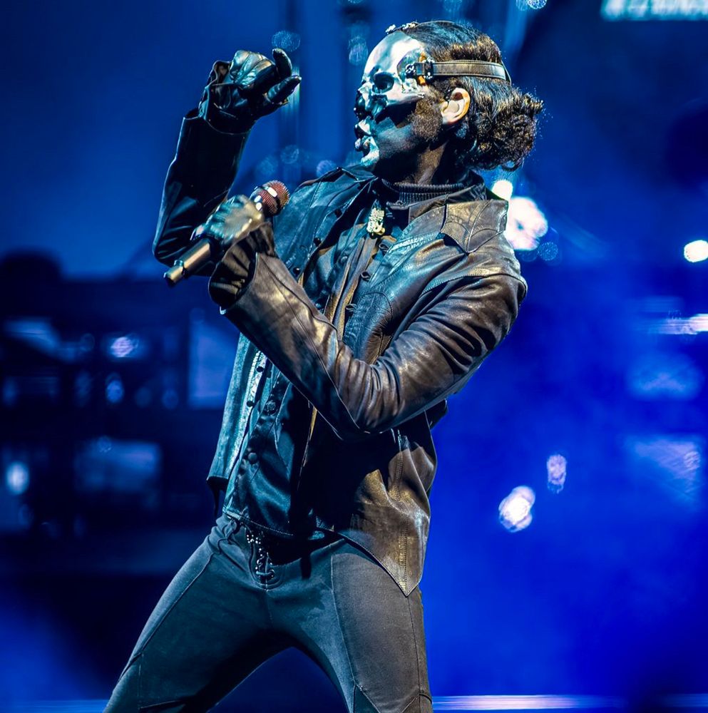 Papa V Perpetua pointing while singing, wearing his leather jacket ensemble while in blue lighting and background