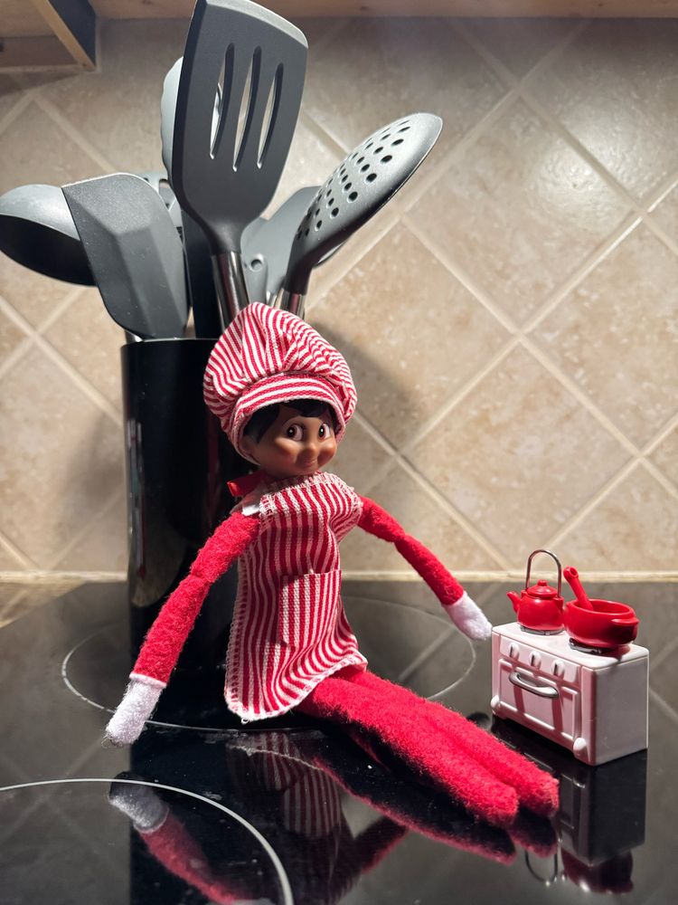 Elf on shelf sitting on stove with a miniature stove and pots. 