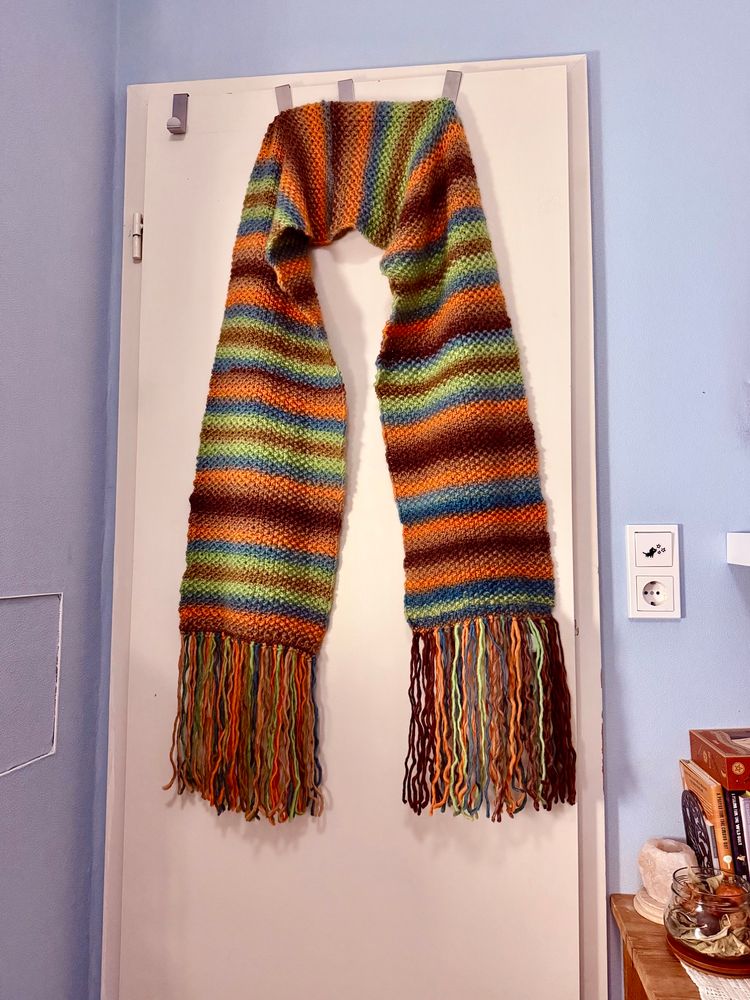 Photo of a large, striped, knitted scarf hung over a door for scale. 