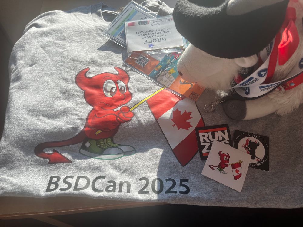GroffTheBSDGoat waking to day 2 of @bsdcan with a selection of the stickers available at registration while staying cozy with the BSDCan 2025 t-shirt