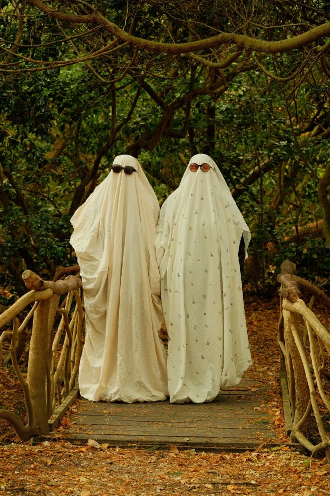 2 people dressed as ghosts stand side by side on a bridge. (Colour photo) 