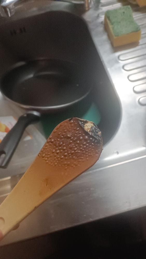 Una espátula de plástico que se ha quemado en una sartén. Está oscurecida y tiene burbujas en la superficie. La punta se ha resquebrajado y se puede ver un plástico poroso en el interior