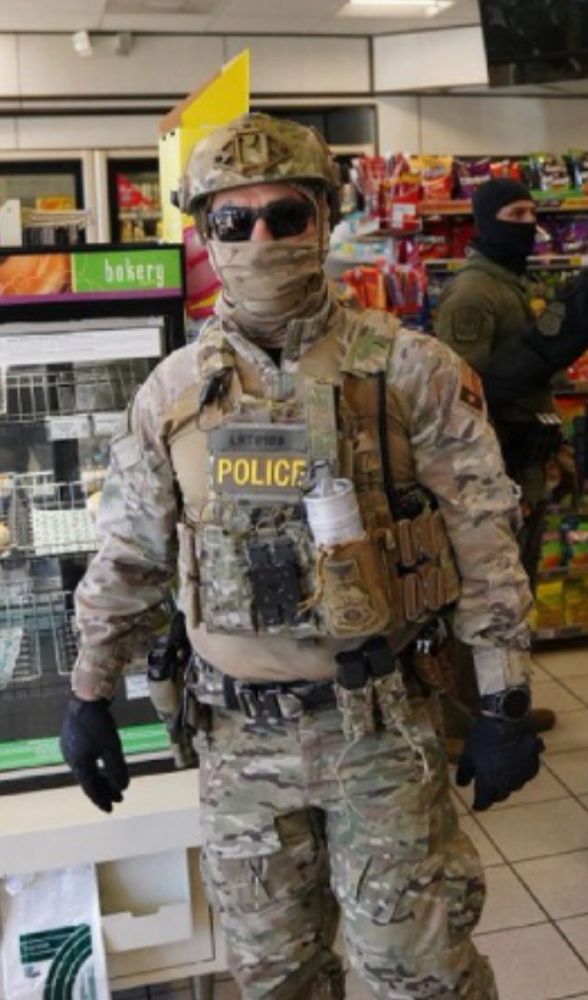 Federal agent in full camp, face mask, helmet and sunglasses, standing in a gas station 