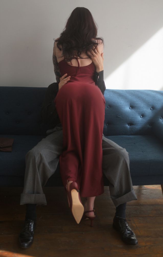 Femme in a red dress being embraced by a man on a couch in a suit
