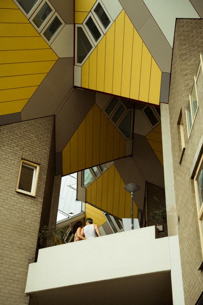 A couple on the edge of a white concrete balcony, framed by the brick pillars and the yellow cubic houses