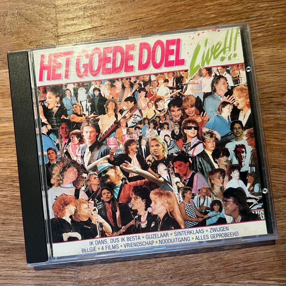 Voorkant van de CD “Het Goede Doel Live!!!” met een collage van livefoto’s van bandleden in expressieve poses. De titel staat bovenaan in felroze en groen. Onderaan staan in blauwe letters de titels van nummers zoals “IK DANS, DUS IK BESTA”, “BELGIË” en “ALLES GEPROBEERD”.

“Eenvoud is onuitputtelijk.“ ~ Krishnamurti
