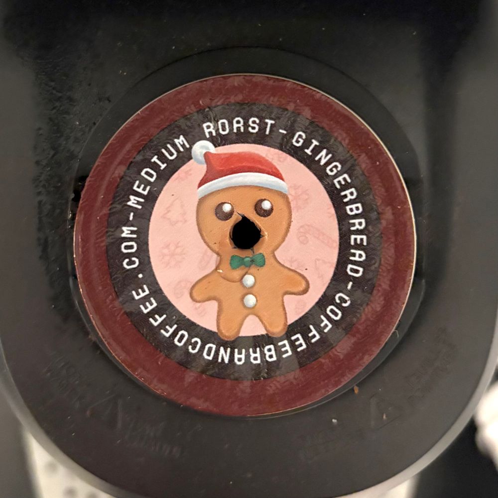 The art on top of the same coffee k-cup from Coffee Brand Coffee as in the previous photo, but the Keurig machine’s puncture hole in the top of the k-cup makes the gingerbread man look like he is crying out in agony with his mouth wide open and drooling.