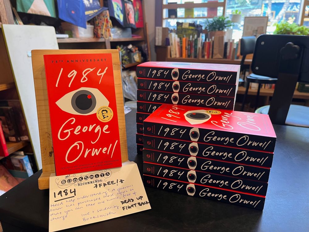 a stack of copies of george orwell's 1984 on our counter with a handwritten sign saying they're free, plus the tagline 'read up fight back'