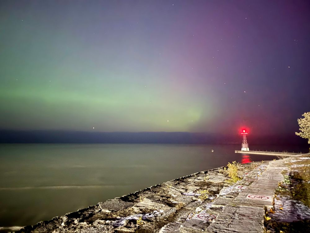 Long exposure picture of a pier off Lake Michigan where you can see a green aurora and the red light of a small lighthouse