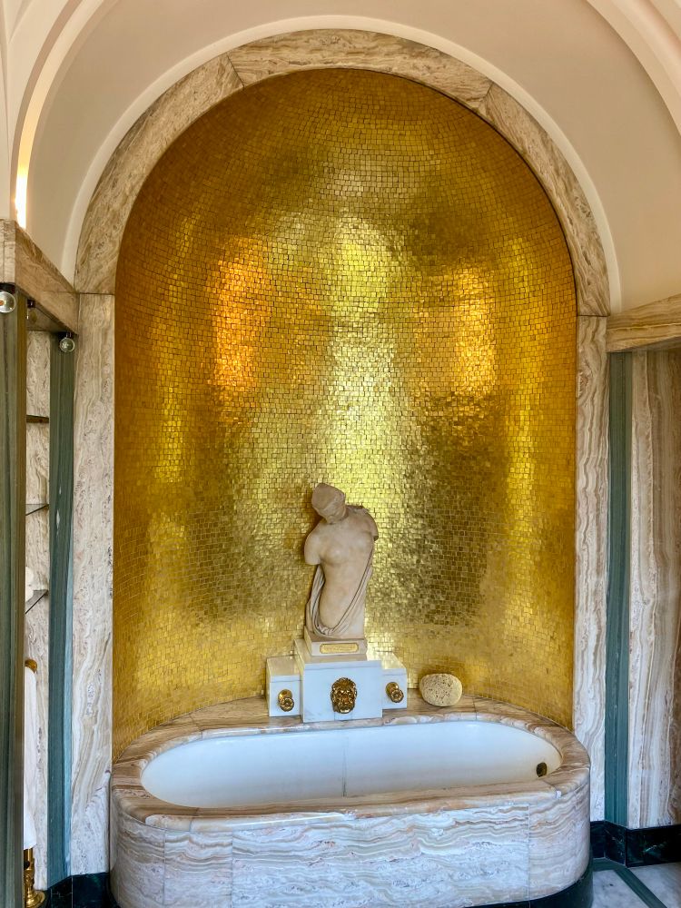 The extravagant bathroom of Lady Virginia Courtauld, complete with a marble bathtub set into a gold-tiled niche in the wall, overlooked by a statue of Psyche.