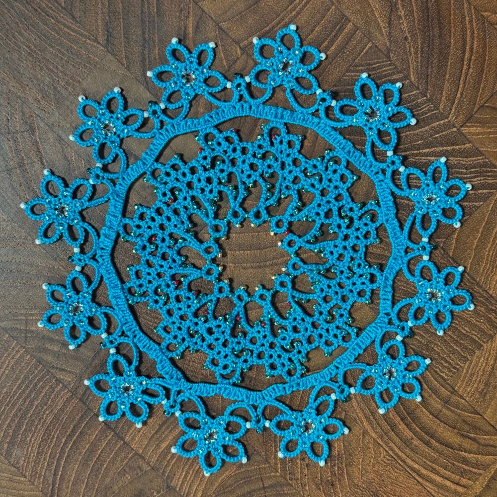 A complex teal-blue doily made with shuttle tatting, a technique to make lace.